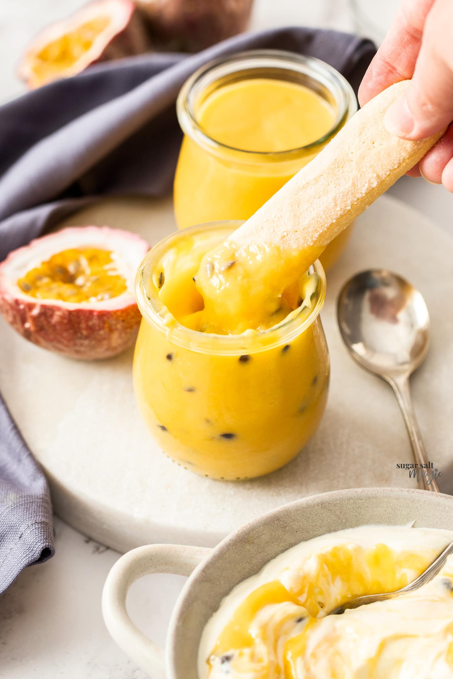 A sponge finger being dipped into passionfruit curd.