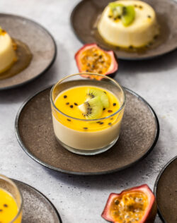 Panna cotta in a glass topped with passionfruit syrup and kiwi fruit slices.