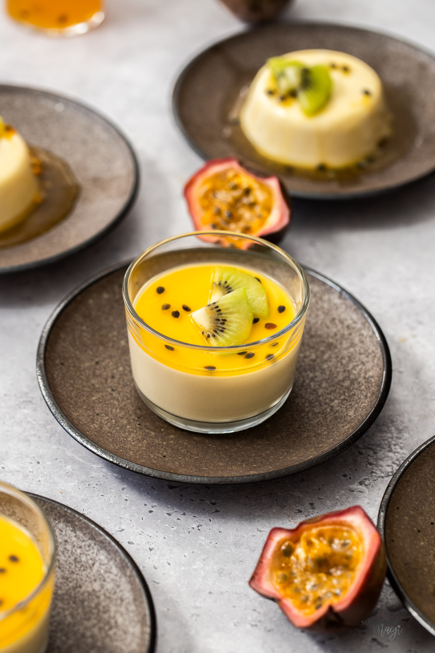 Panna cotta in a glass topped with passionfruit syrup and kiwi fruit slices.