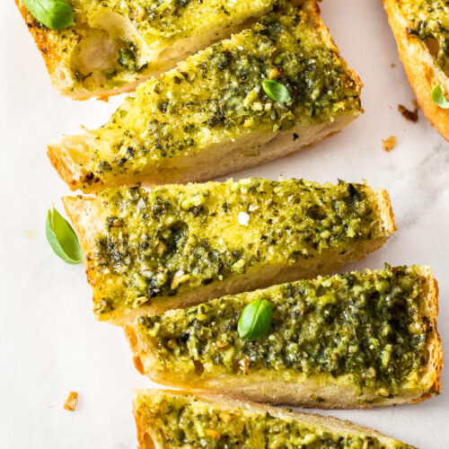 Slices of pesto garlic bread on a sheet of baking paper.