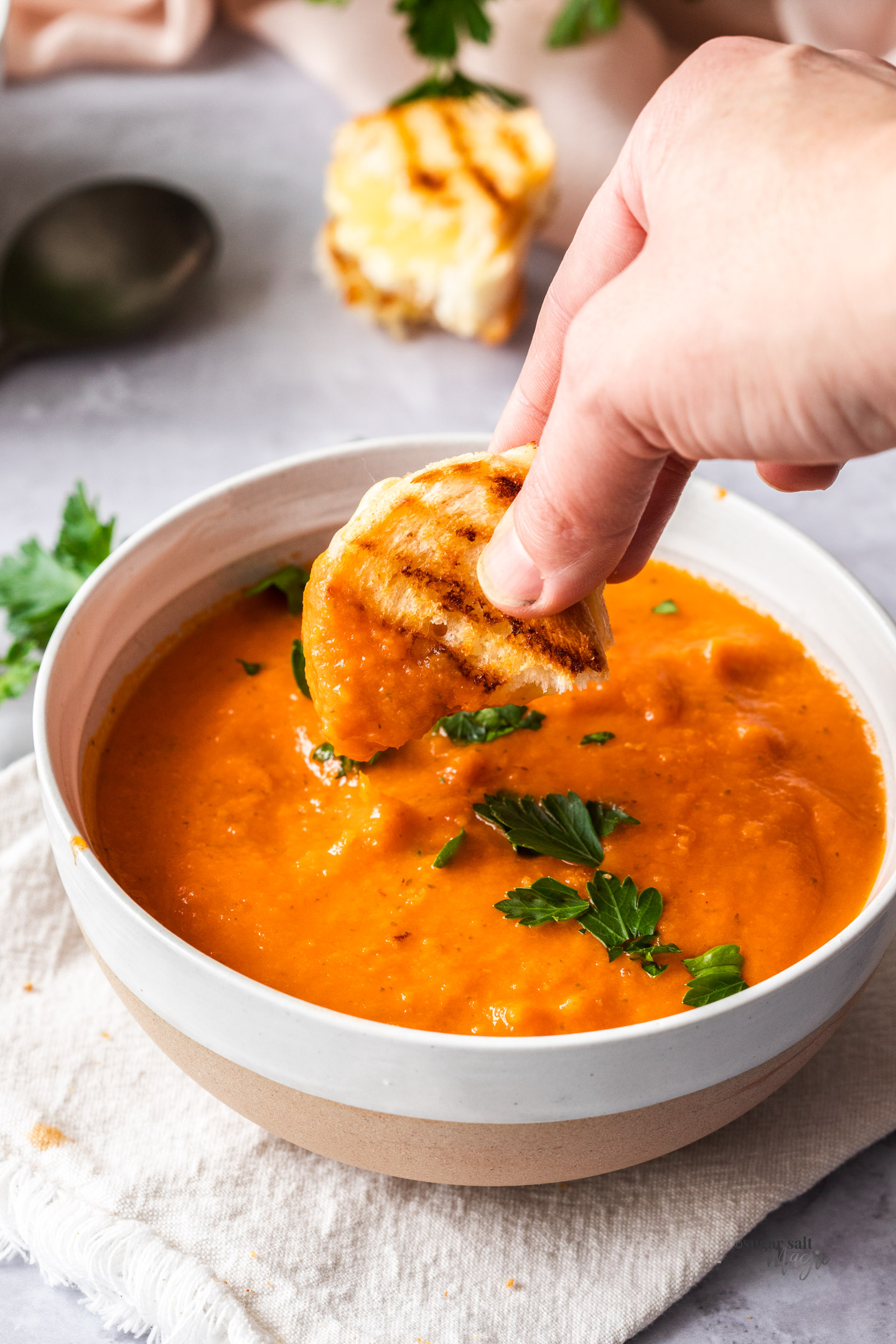 A mini grilled cheese being dipped into a bowl of tomato soup.