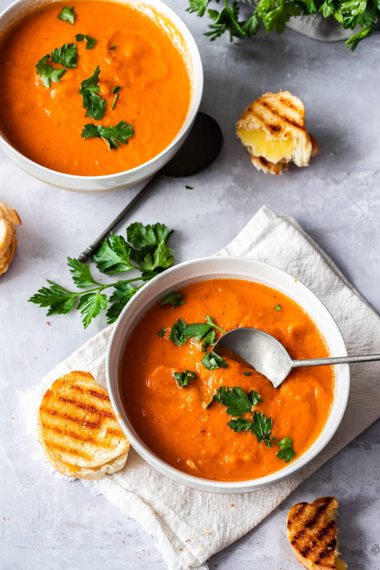 Two bowls of tomato soup surrounded by mini grilled cheese sandwiches.