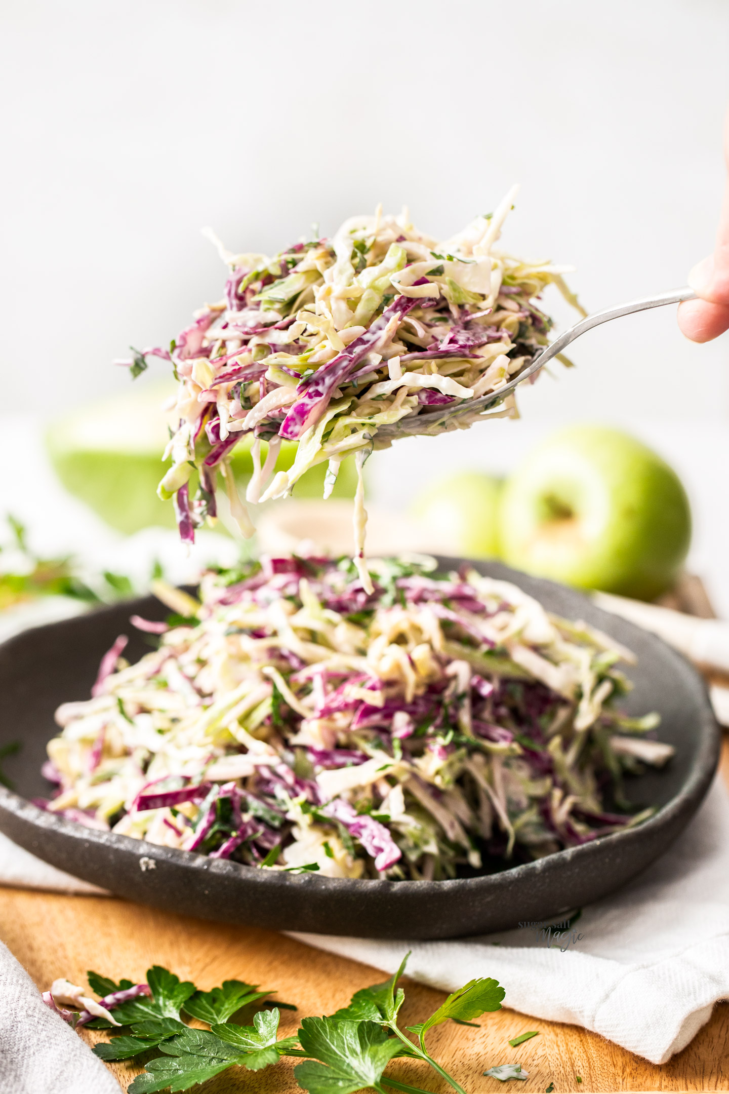 Apple coleslaw being taken from a dish on a spoon.