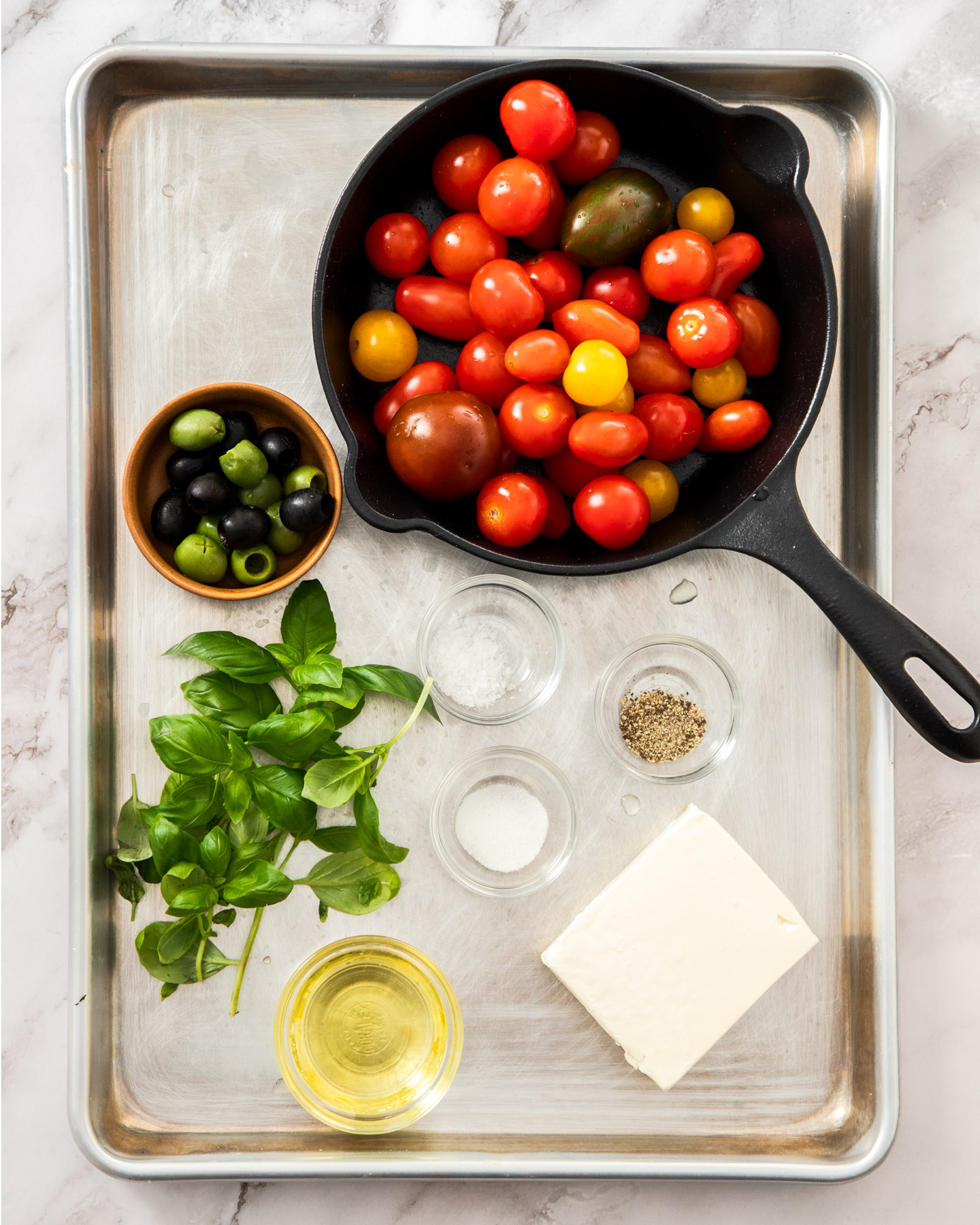 Ingredients for baked feta and tomatoes on a metal tray.