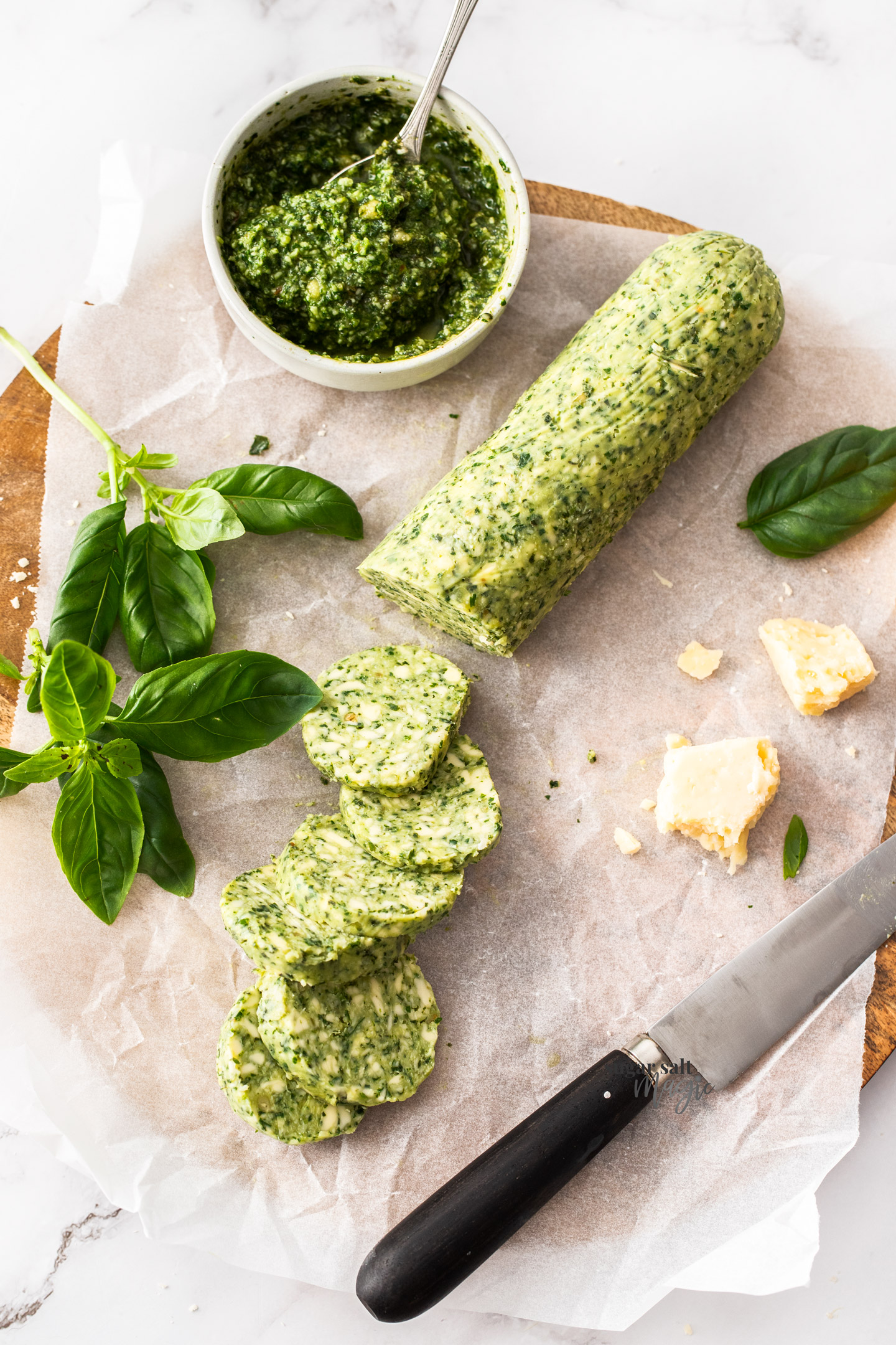 A log of pesto butter on a chopping board with some disks cut from it.