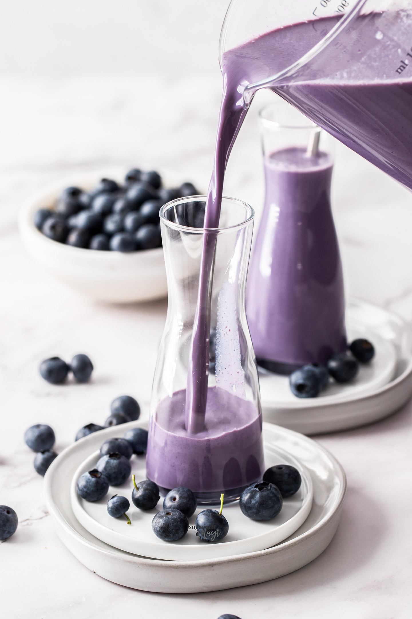 A tall glass being filled with blueberry milk.