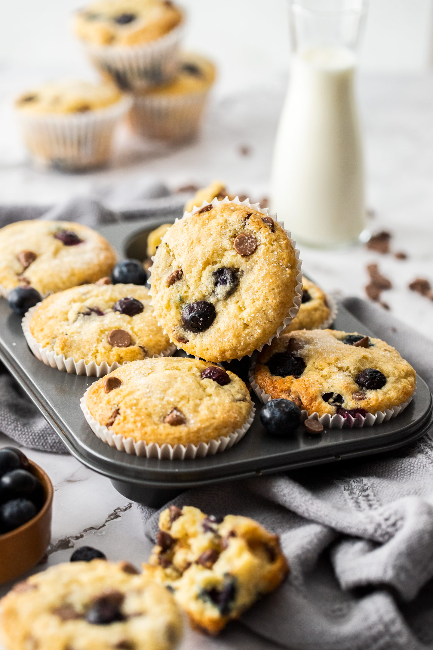 A muffin tin filled with baked blueberry muffins with one sitting on top.