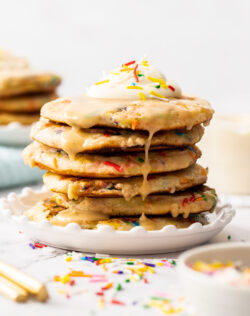 A stack of funfetti pancakes with cream on top and glaze.