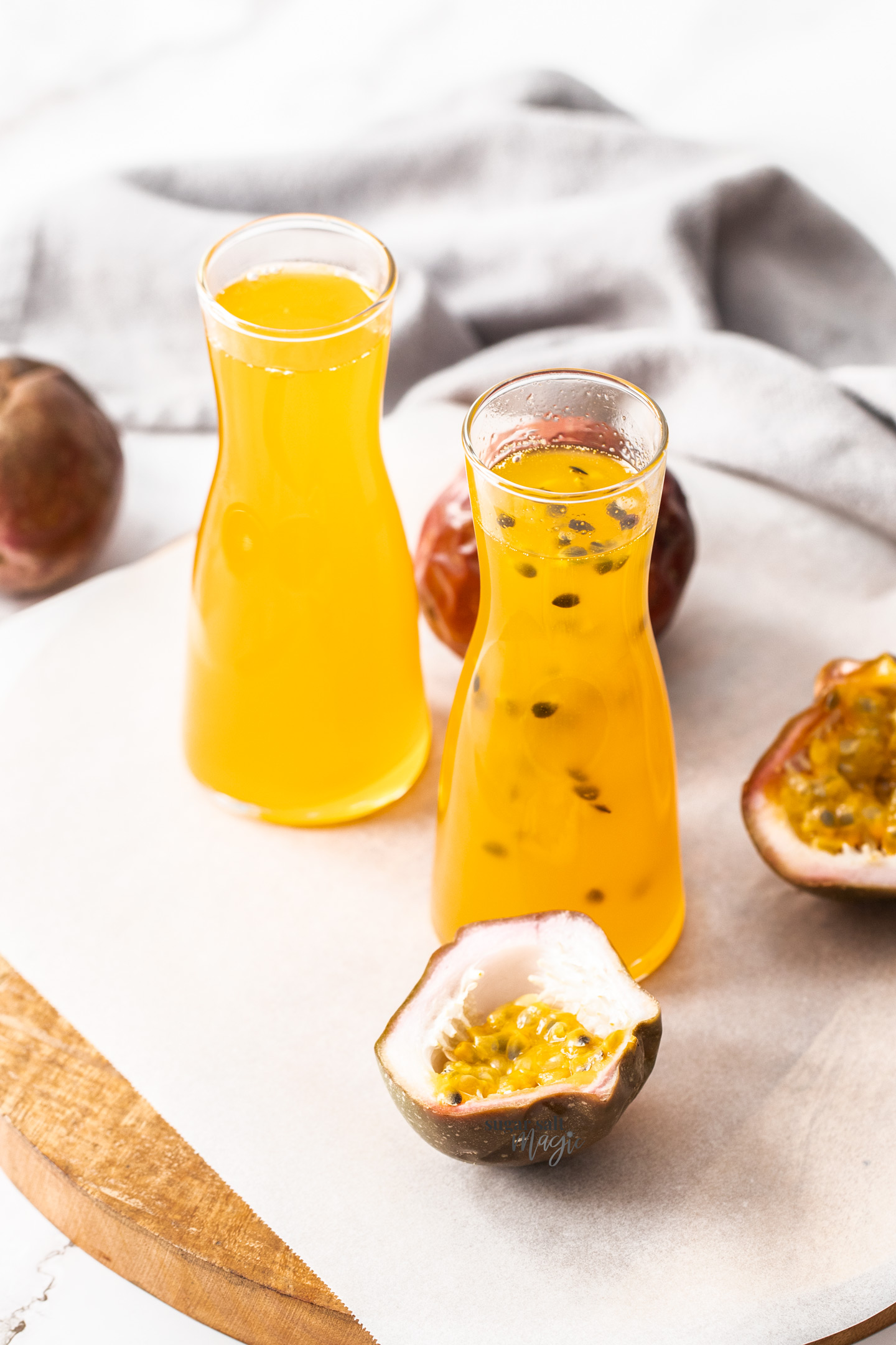 Two bottles of passionfruit syrup surrounded by passionfruits.