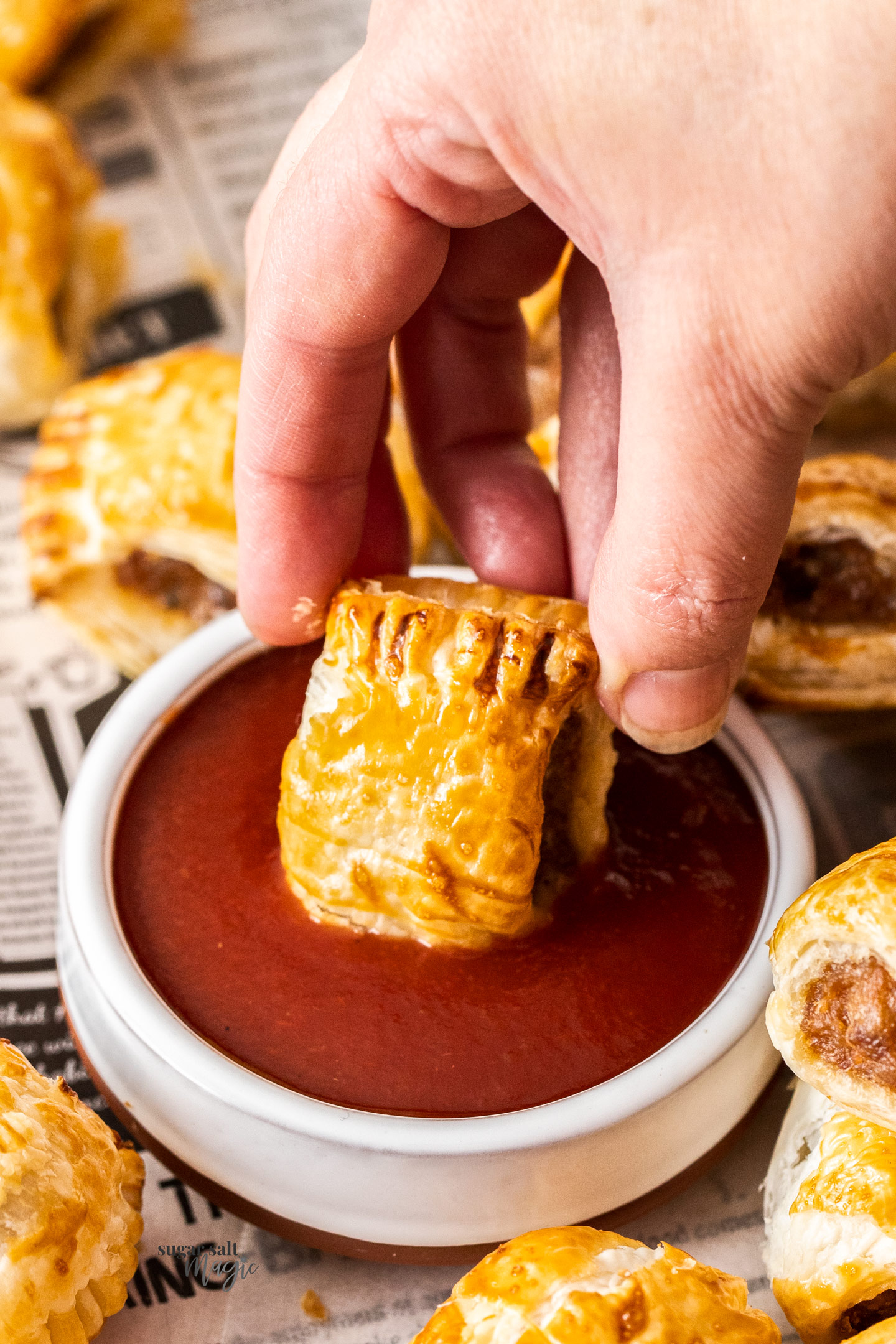 A sausage roll being dunked into ketchup.