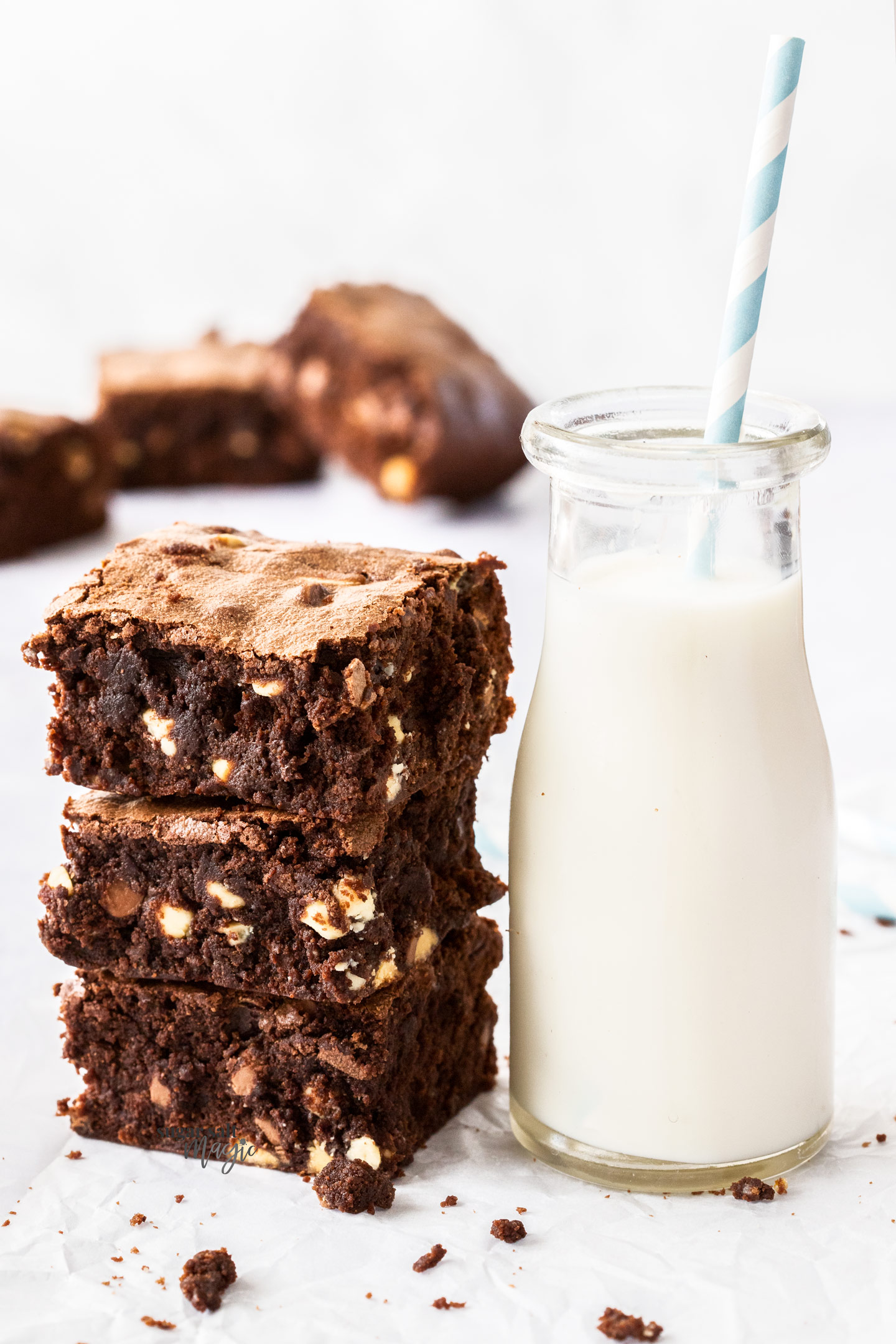 A stack of 3 brownies next to a small bottle of milk.