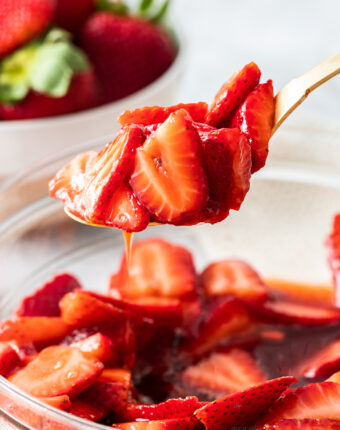 Macerated strawberries on a spoon being lifted out of a bowl.