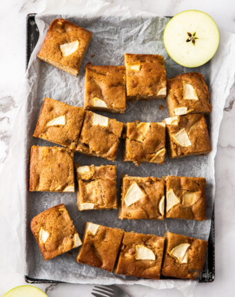 An apple traybake cake cut into squares on a baking tray.