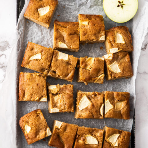 An apple traybake cake cut into squares on a baking tray.