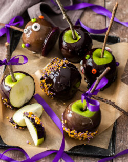6 black candy apples on a tray, one cut into pieces.
