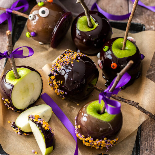 6 black candy apples on a tray, one cut into pieces.