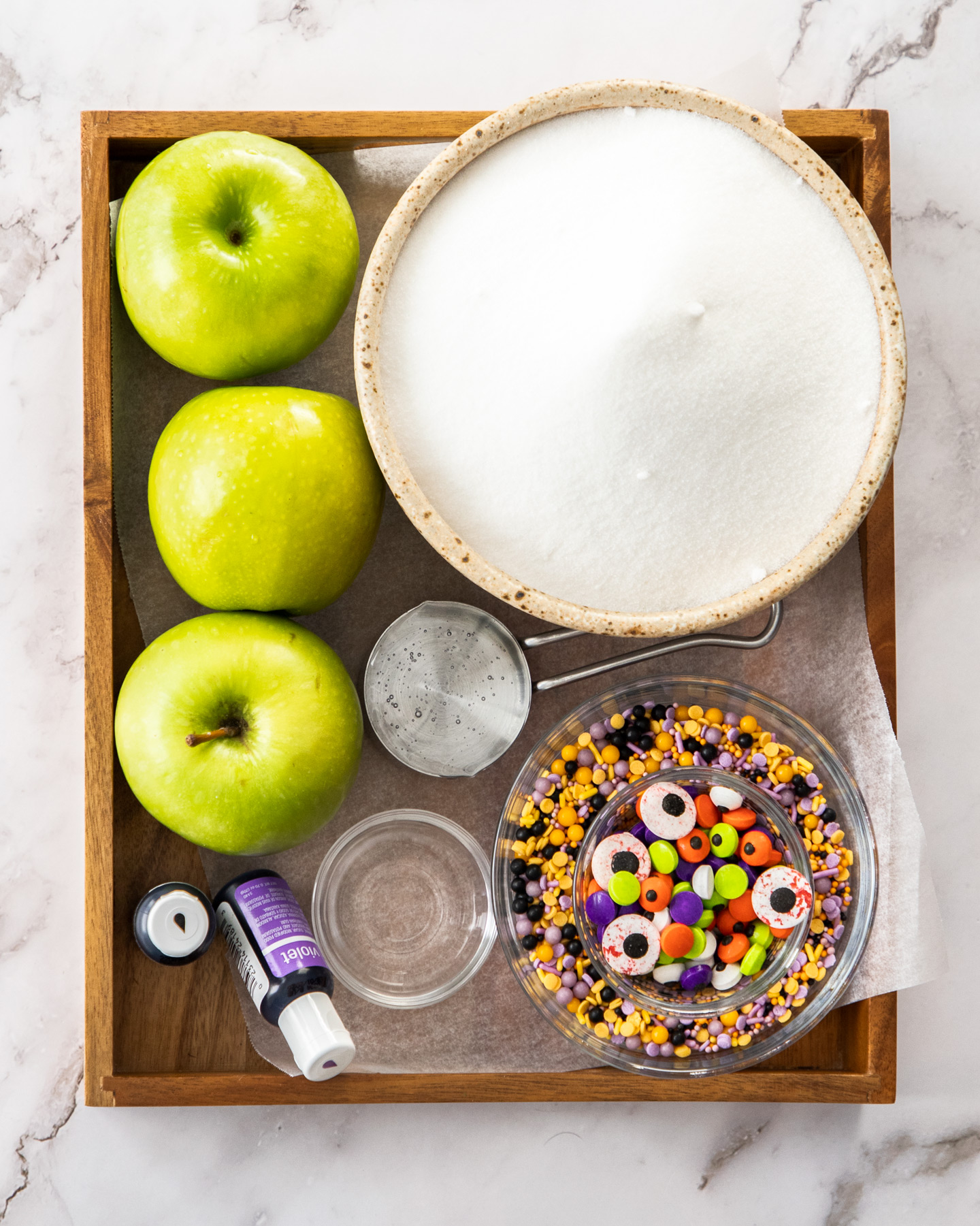 Ingredients for halloween candy apples on a wooden tray.