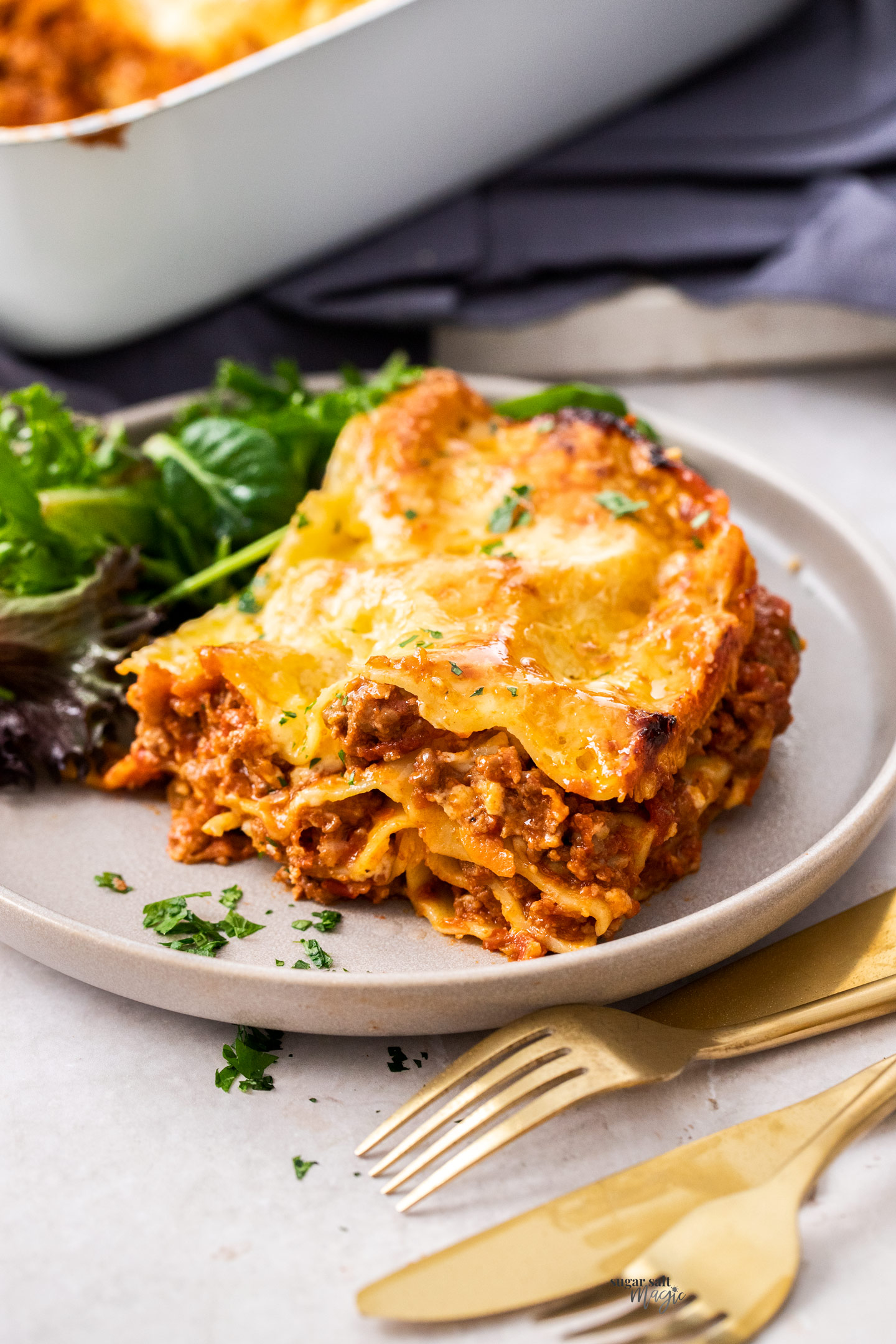 A slice of lasagna on a plate with salad.
