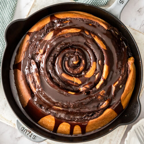 Top down view of a chocolate scroll coated in chocolate sauce.