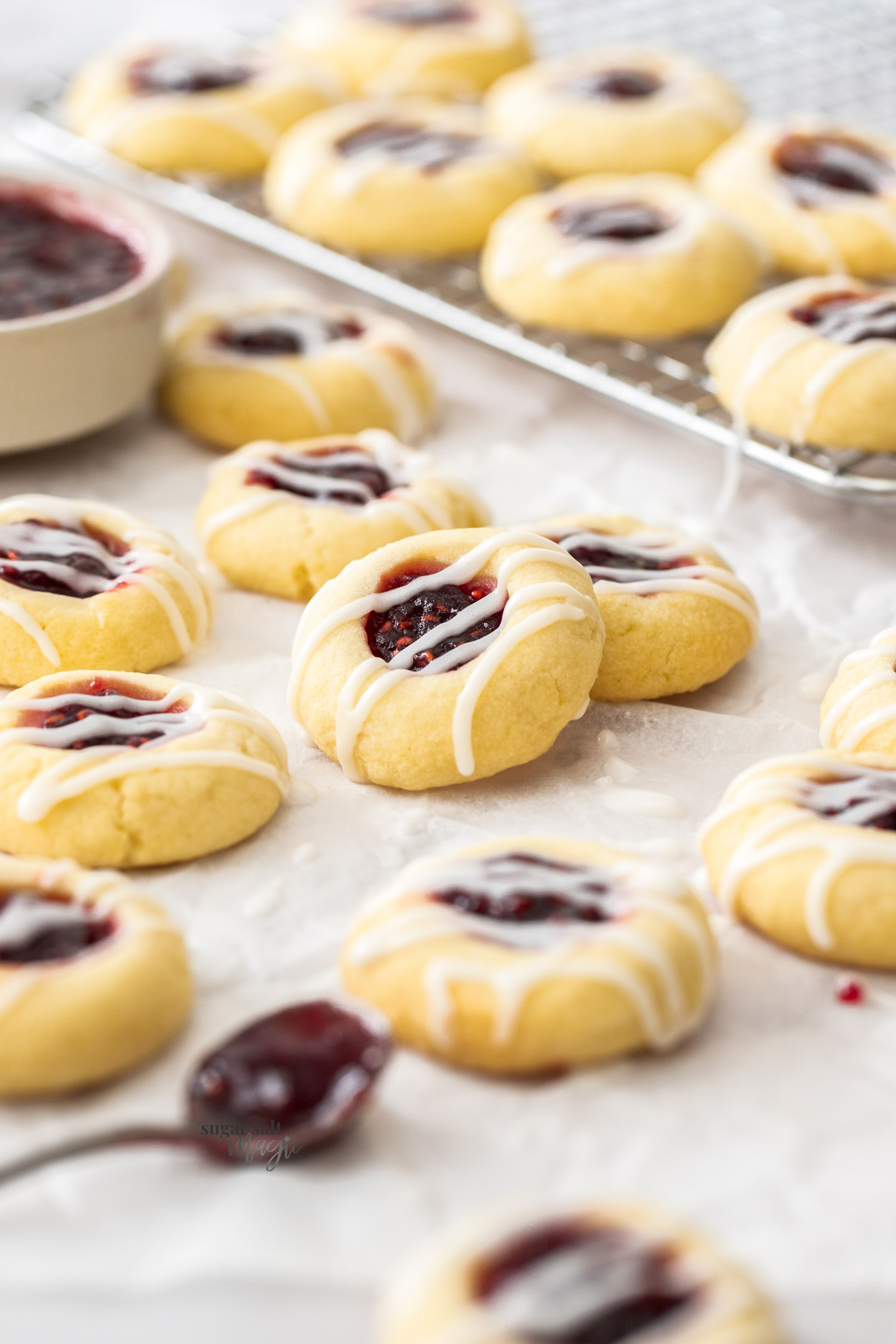 A batch of jam thumbprint cookies on a sheet of baking paper.