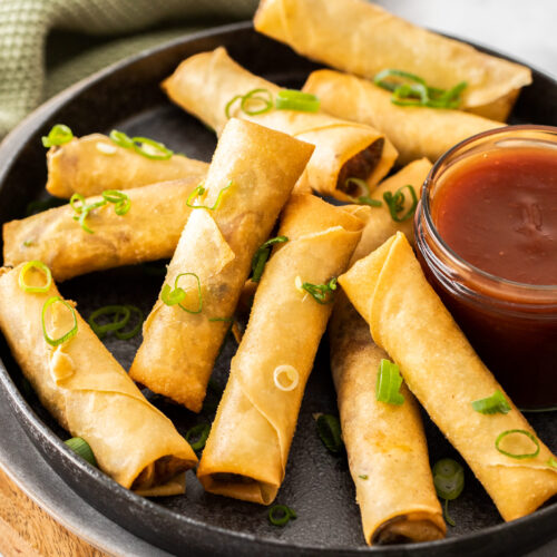 A batch of spring rolls on a plate with sauce.