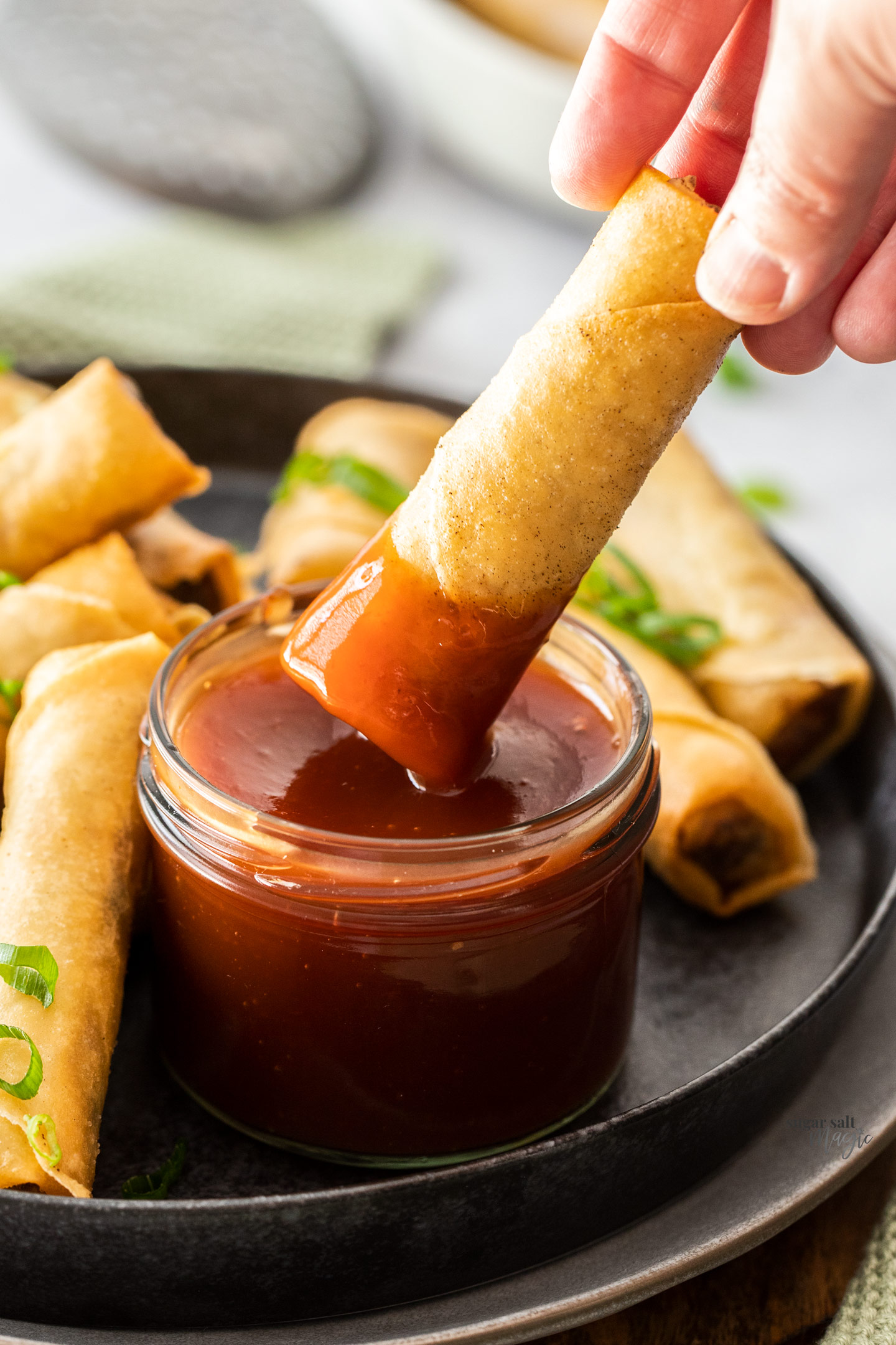 A spring roll being dipped into sweet and sour sauce.