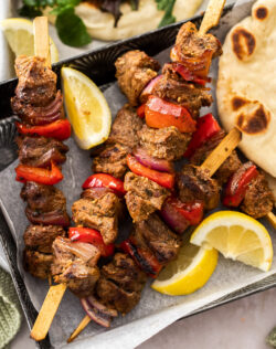 5 Greek lamb kebabs on a dark tray.