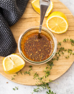Top down view of marinade in a jar with lemons and thyme around it.