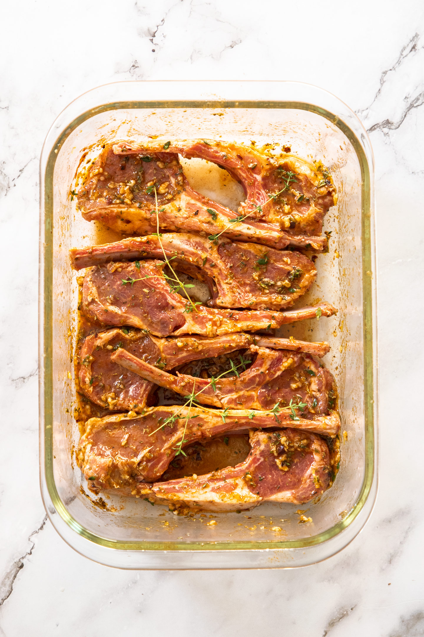 8 lamb chops covered in marinade in a glass dish.