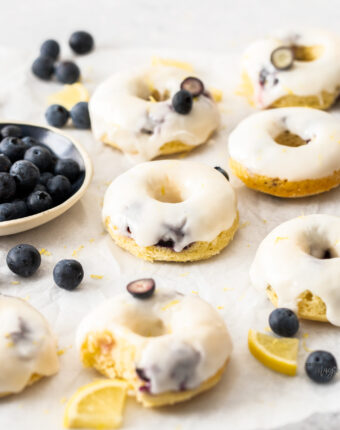 A batch of iced blueberry donuts on a sheet of baking paper.