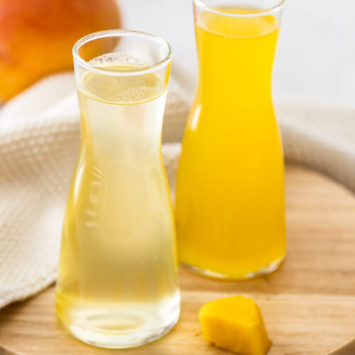 Closeup of two glass bottles of mango syrup on a wooden board.