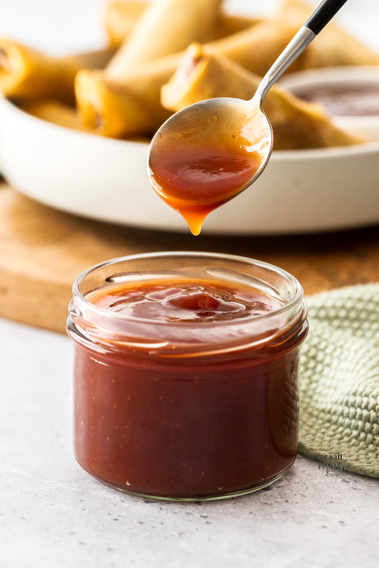 A spoon coming out of a jar with sweet and sour sauce.