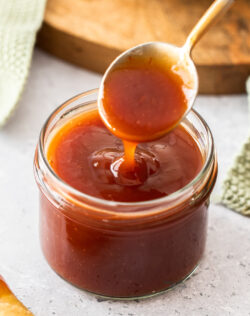 A spoon coming out of a jar with sweet and sour sauce.