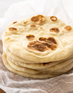 A stack of 6 flatbreads on a wooden board.