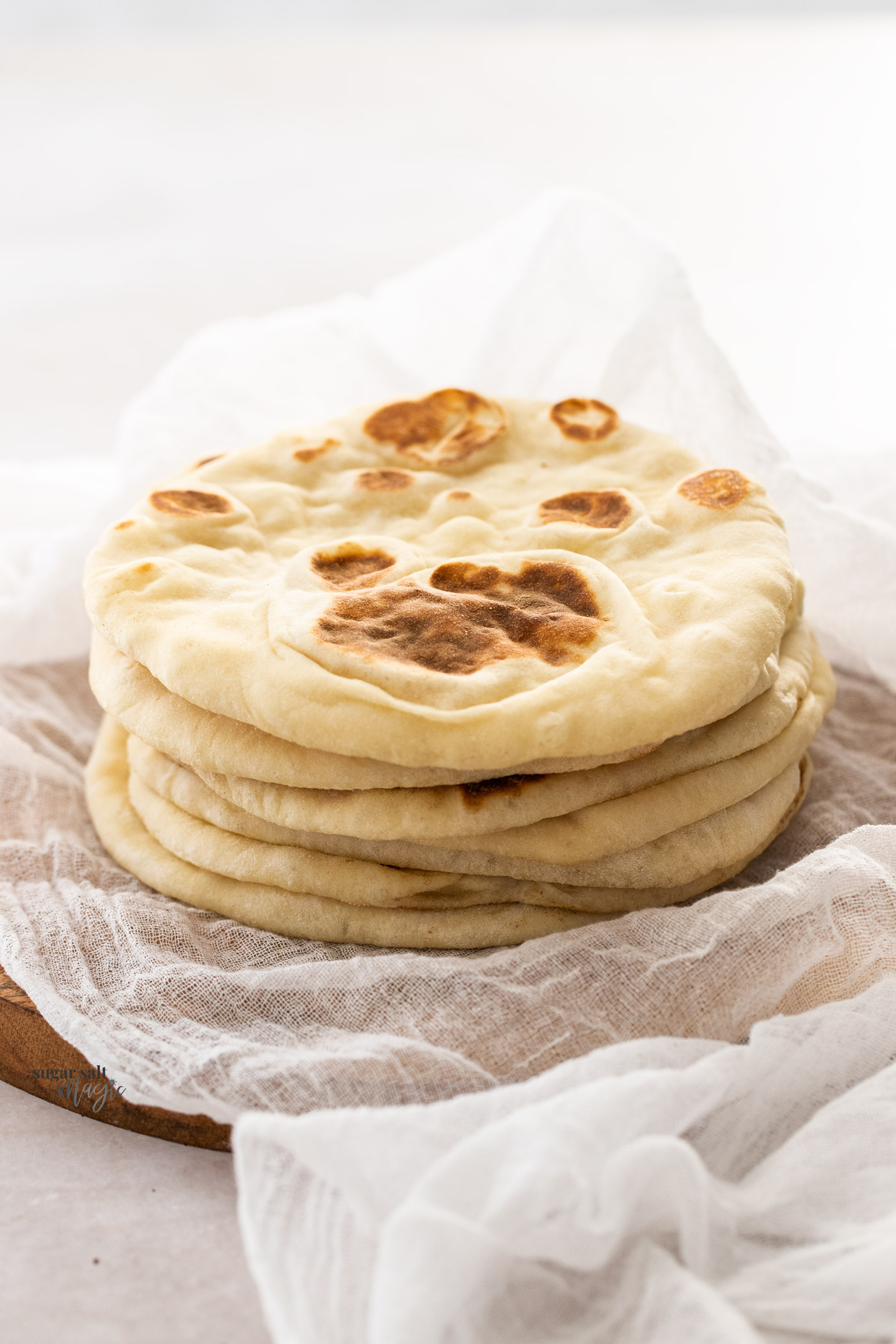 A stack of 6 flatbreads on a wooden board.