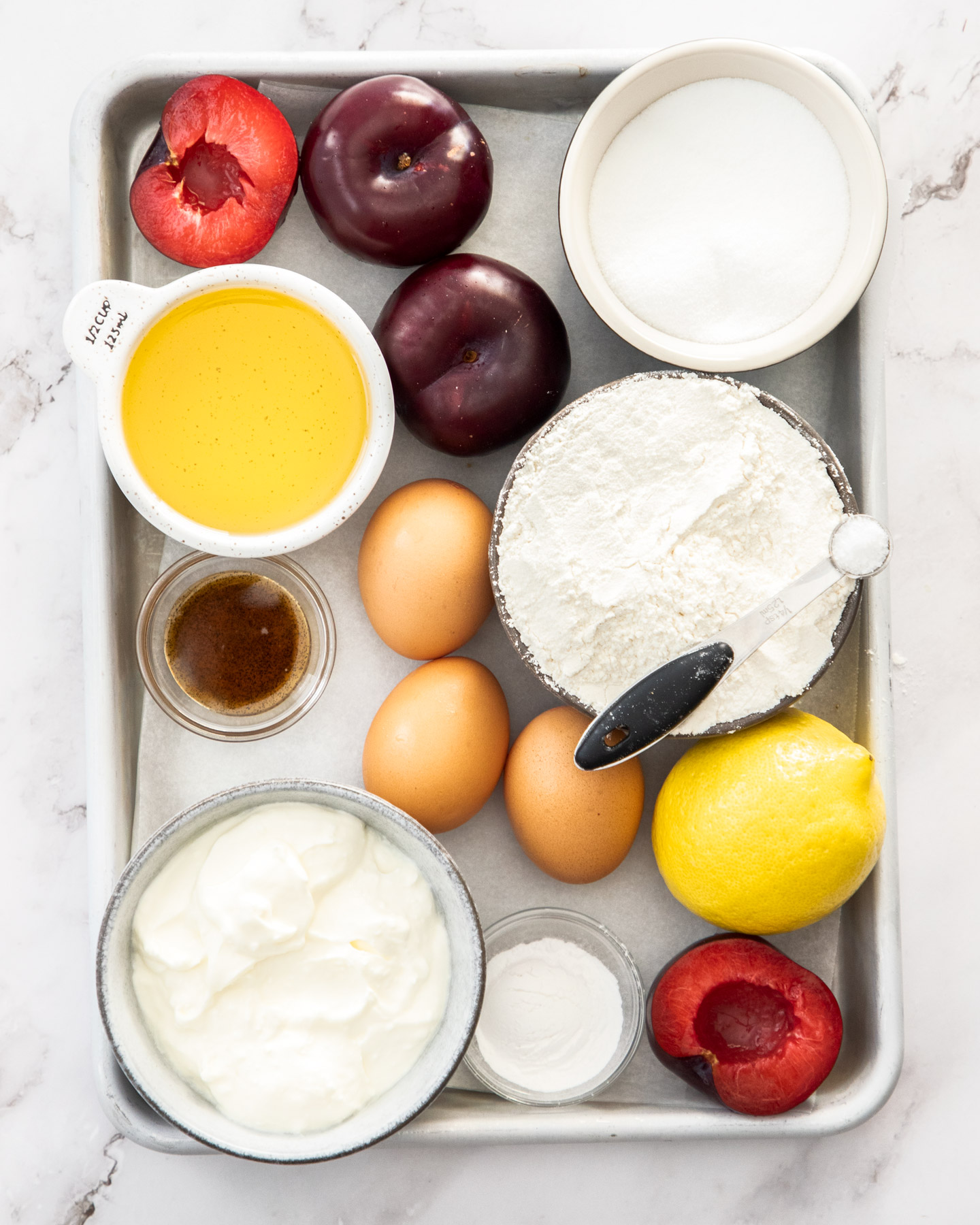 Ingredients for plum cake on a baking tray.