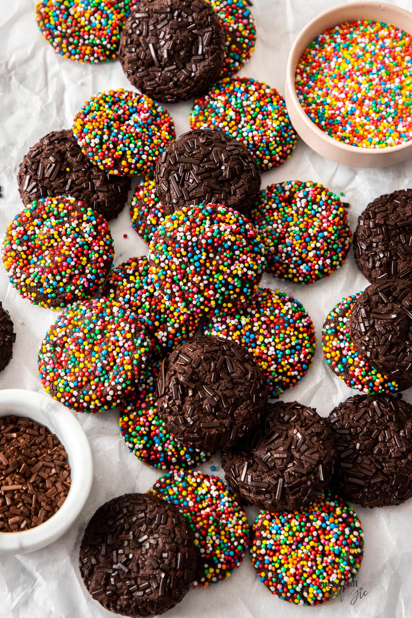A batch of chocolate sprinkle cookies on a sheet of baking paper.
