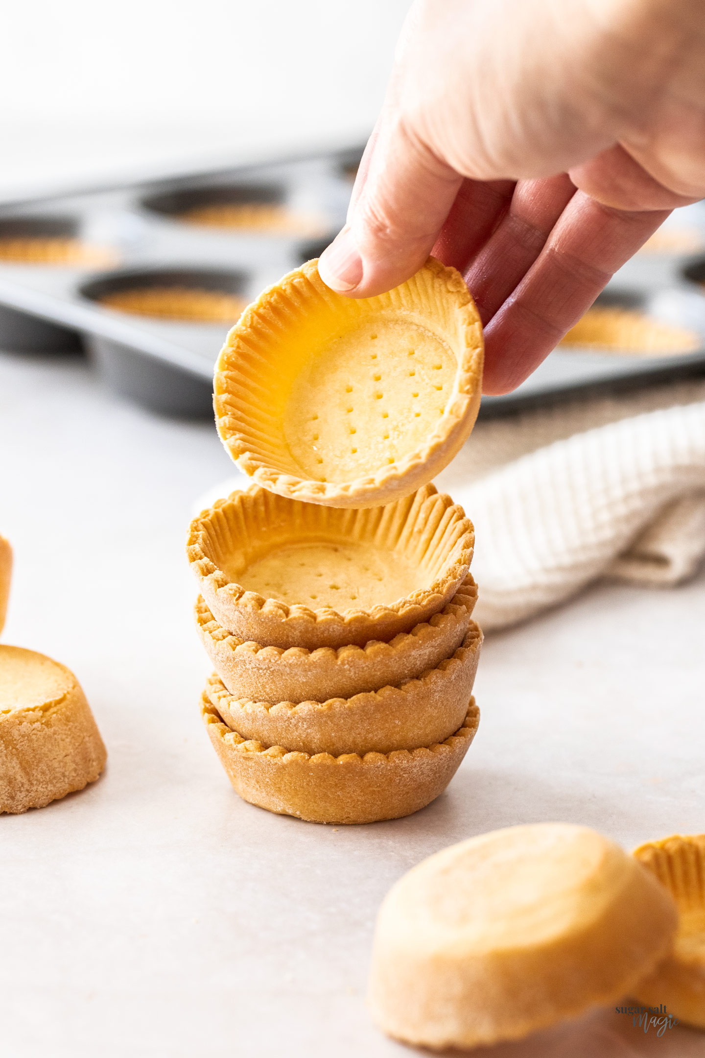A hand picking up a tartlet shell off a stack.