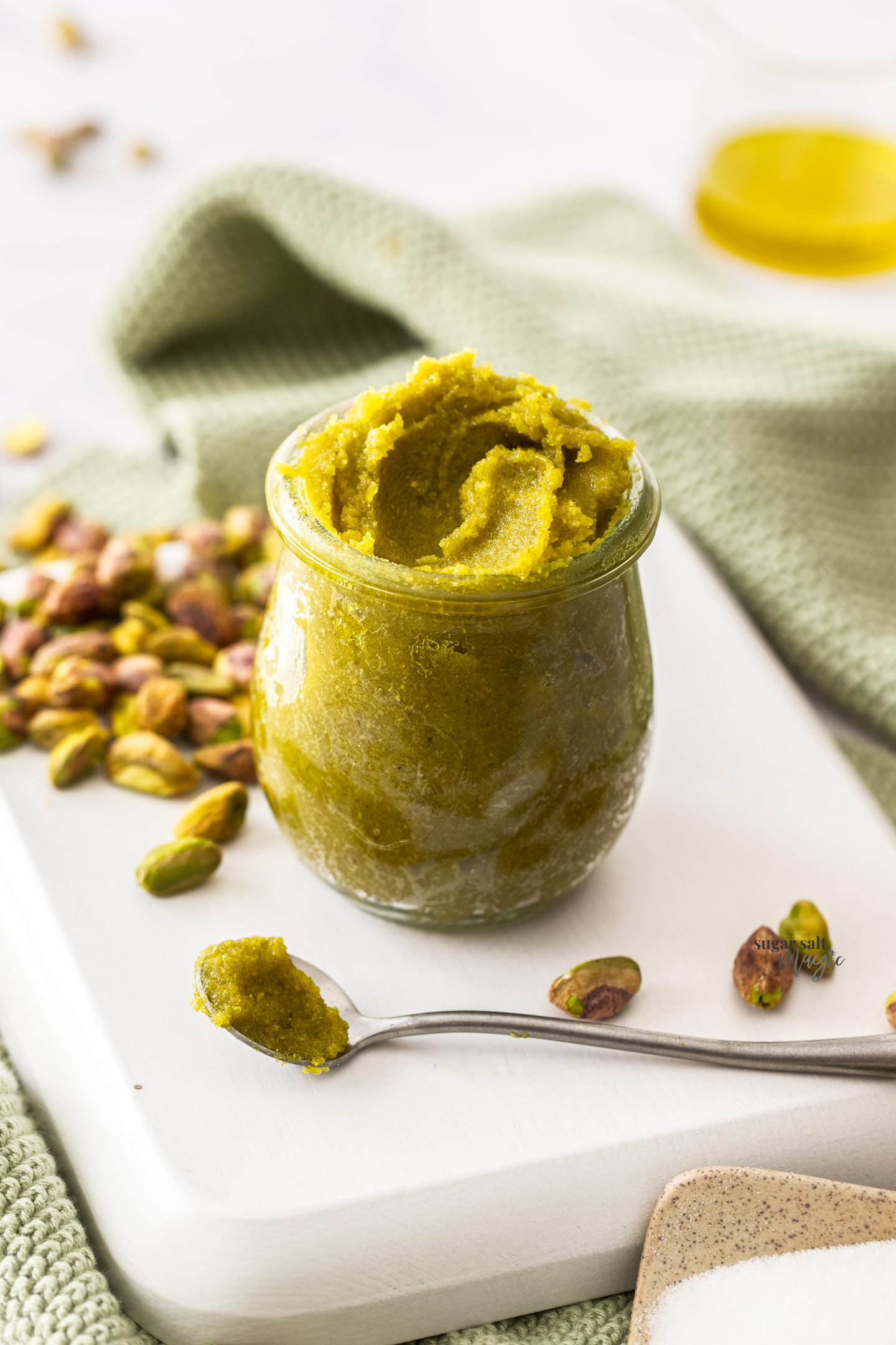 A small jar filled with pistachio paste with pistachios around it.