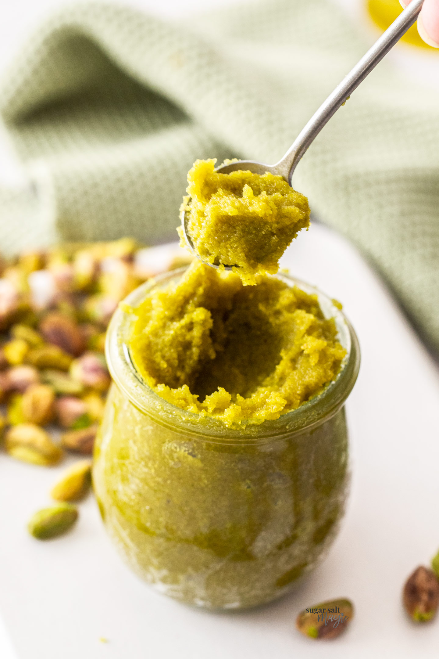 A spoon taking pistachio paste from a jar.