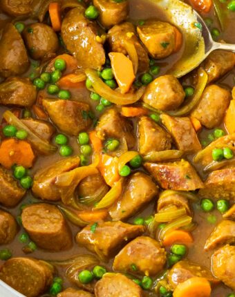 Curried sausages with peas and carrots in a pan.