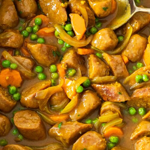 Curried sausages with peas and carrots in a pan.