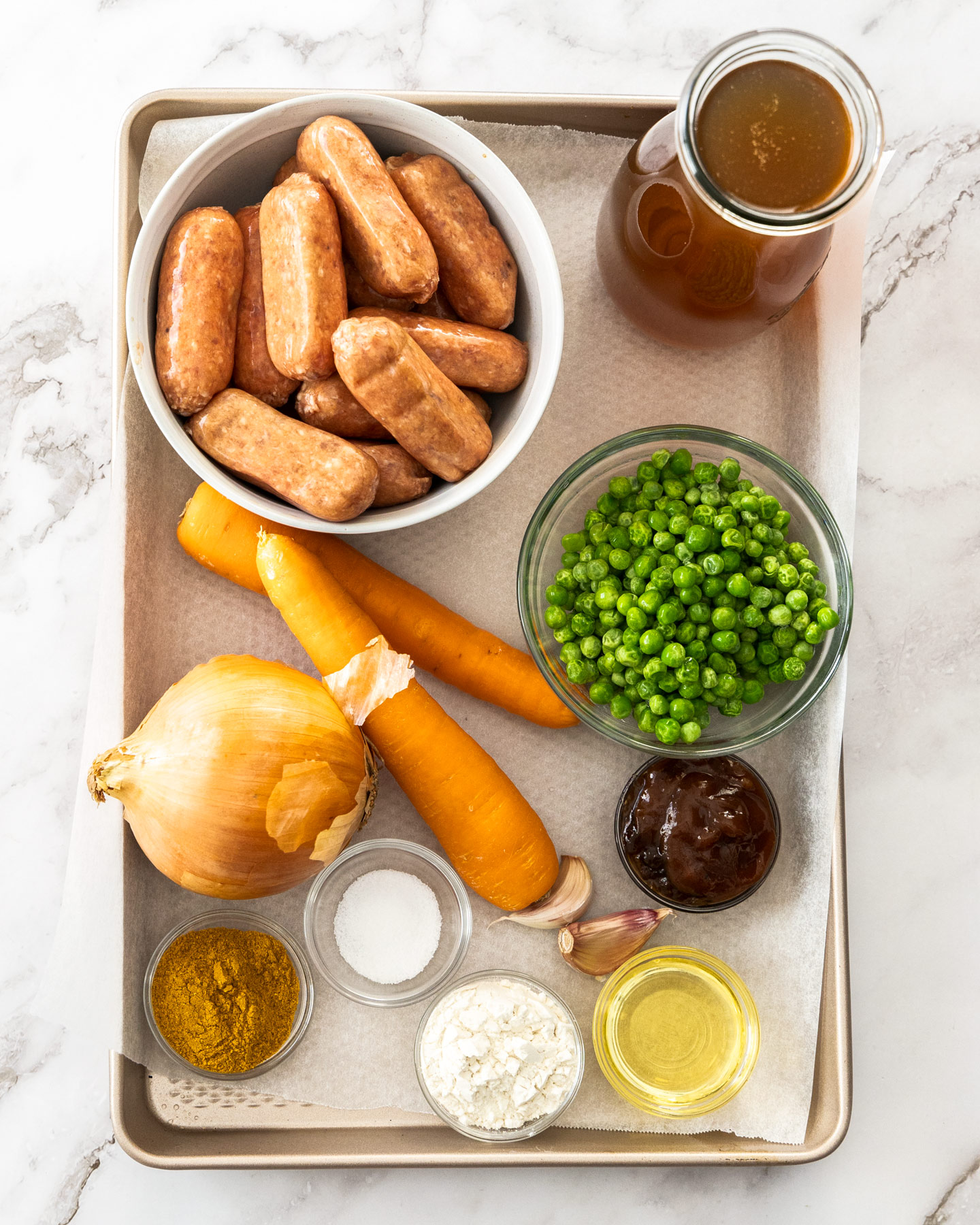 Ingredients for curried sausages on a baking tray.