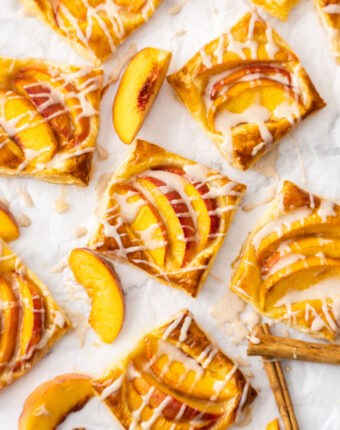 8 mini puff pastry peach tarts on a sheet of baking paper.