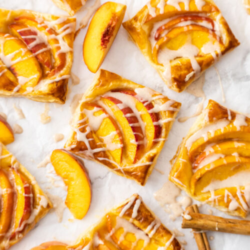 8 mini puff pastry peach tarts on a sheet of baking paper.