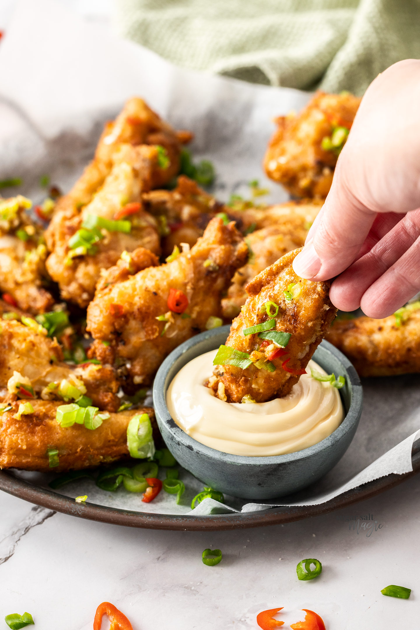 A hand dipping a chicken wing into mayonnaise.
