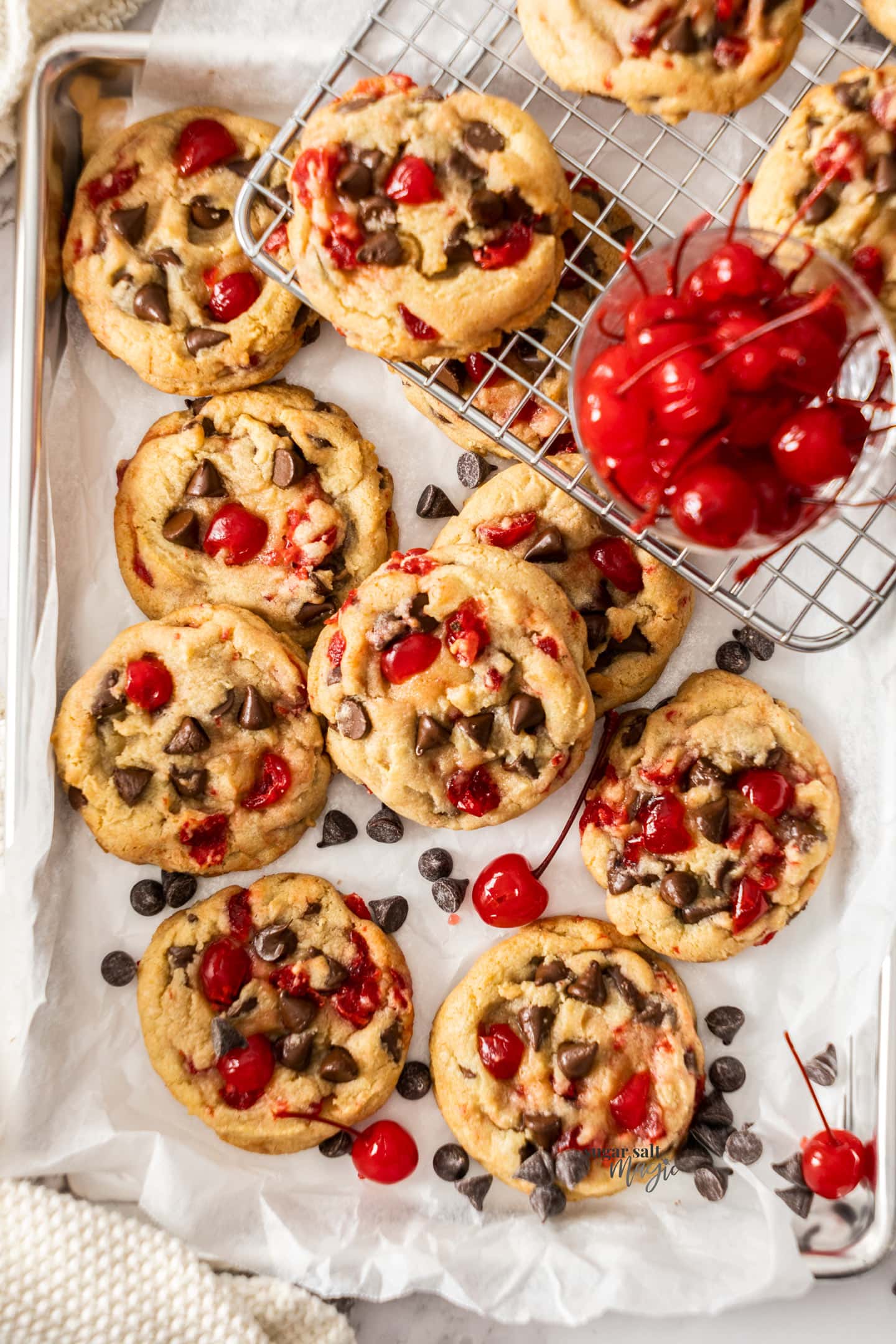 A batch of cherry laden chocolate chip cookies on a baking tray.