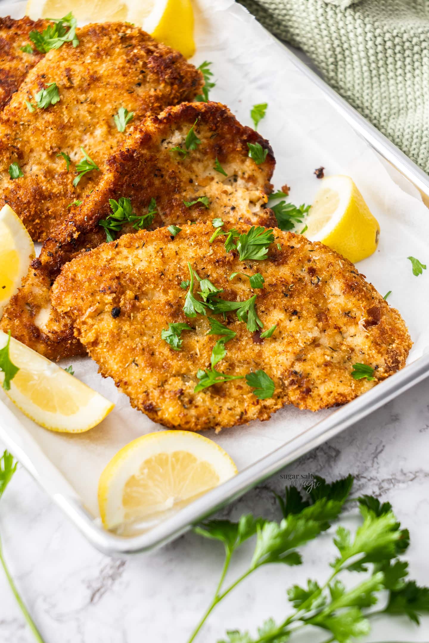 Italian chicken cutlets stacked on a baking tray.