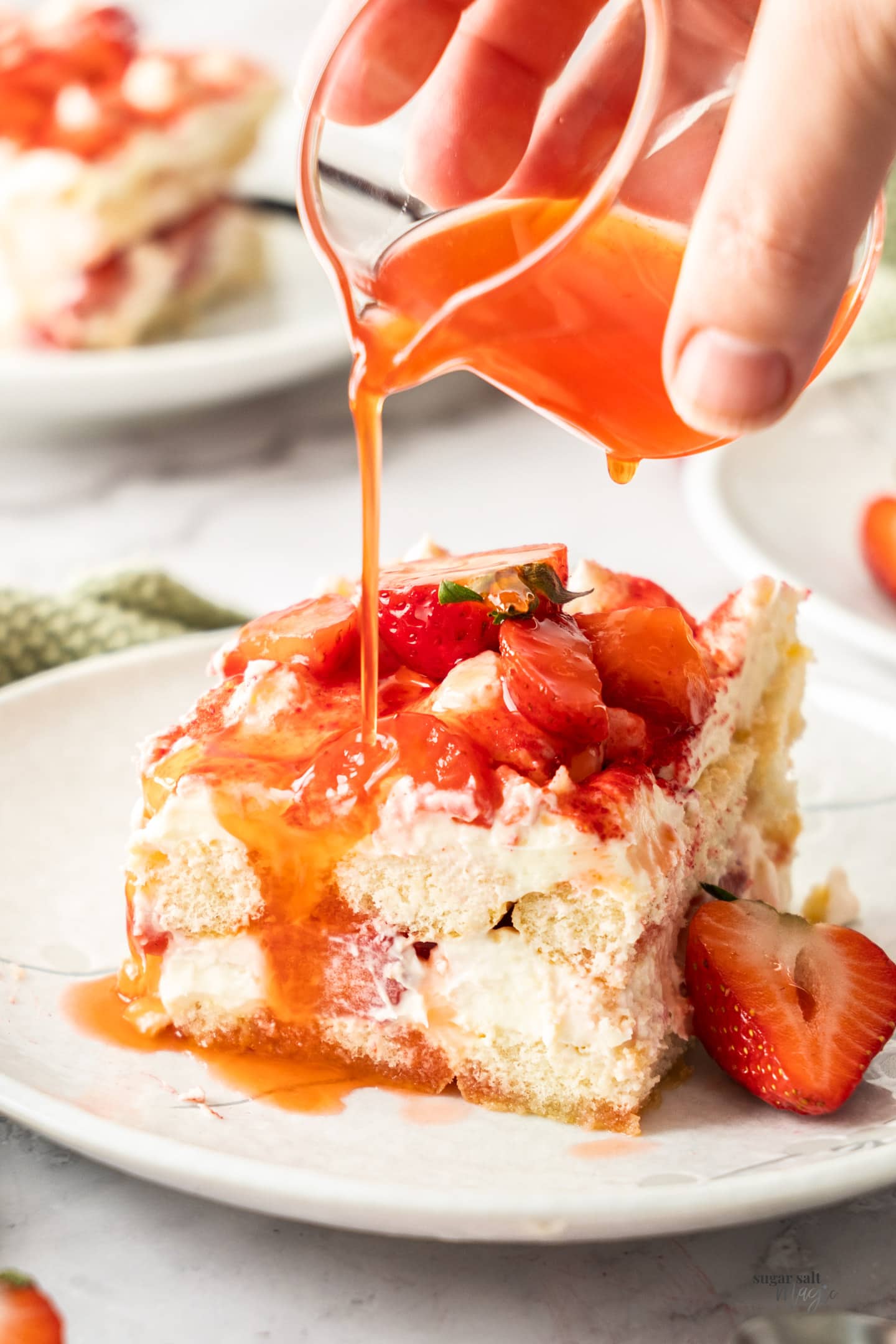 A slice of strawberry tiramisu with syrup being poured over the top.