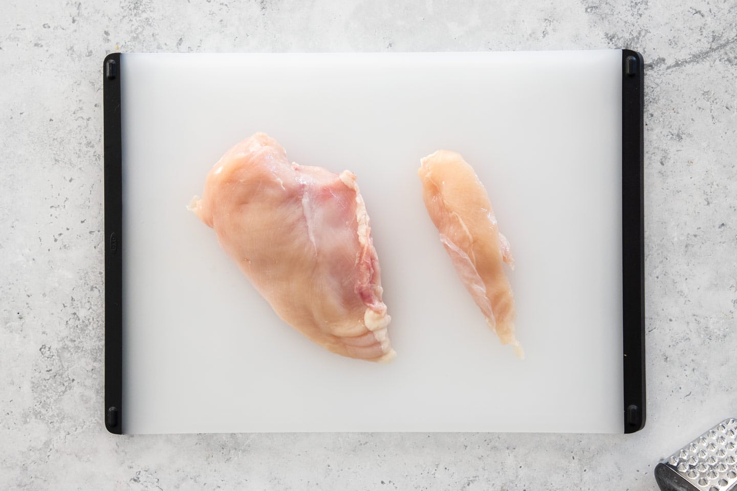 A chicken breast and chicken tender on a chopping board.